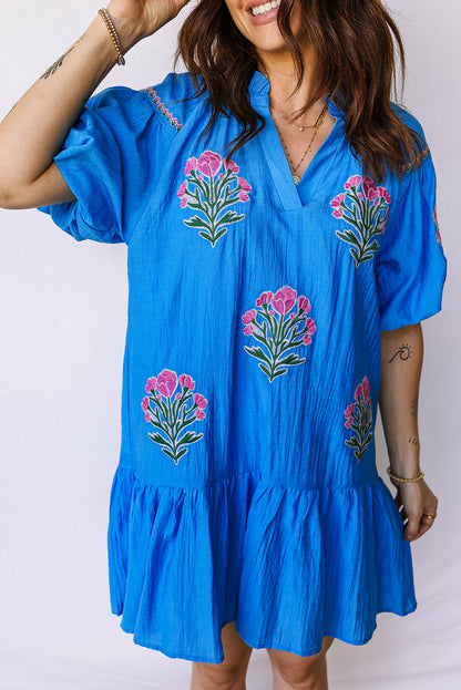 Vestido con bordado de flores azules, cuello dividido, mangas cortas abullonadas y dobladillo con volantes